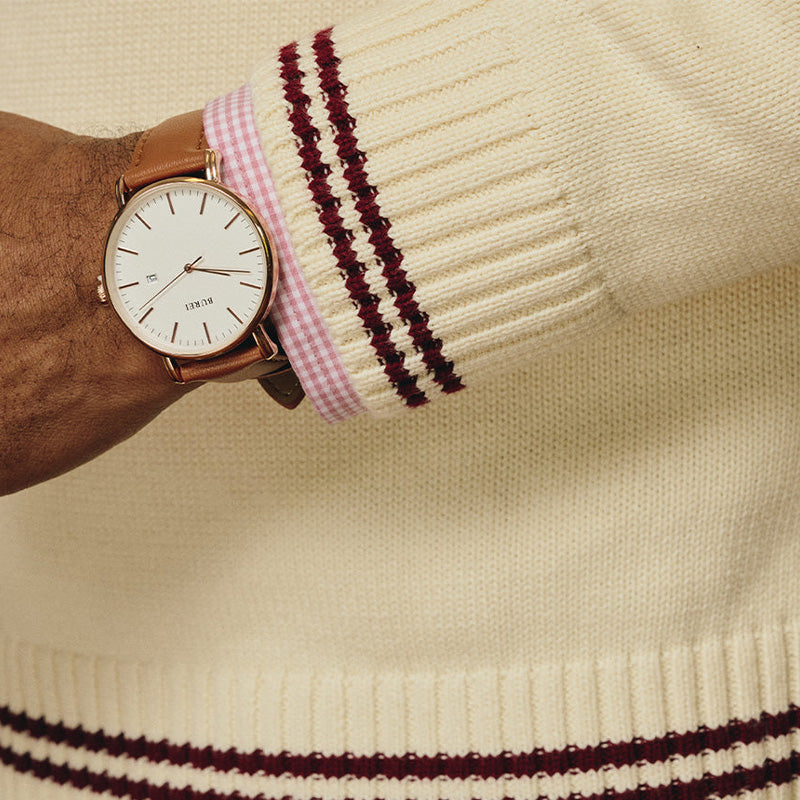 Close-up of a man's wrist showing a watch and the sleeve of a custom Greek embroidery sweater with maroon stripes.