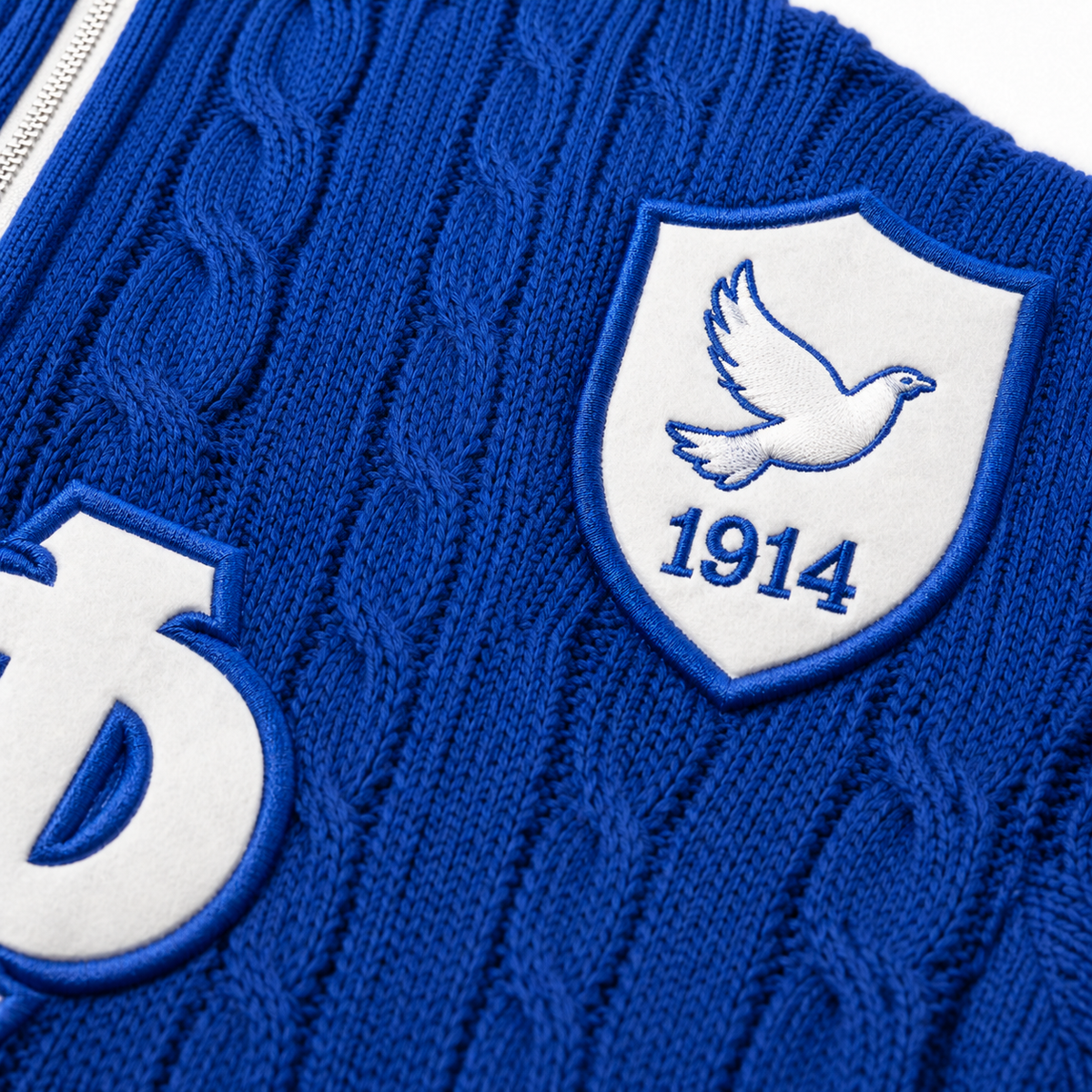 Close-up blue cable knit with white dove shield, 1914 detail, jacquard patches and neat seam finishing