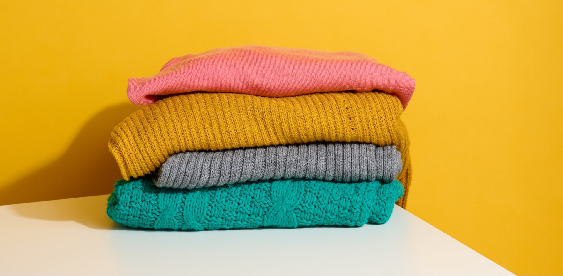 Stack of colorful custom knit sweaters by a custom sweater manufacturer, featuring pink, yellow, grey, and turquoise sweaters designed for bulk production for European and American fashion brands