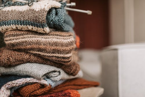 Stack of cozy, high-quality knit sweaters showcasing a variety of yarns like cotton, merino wool, and cashmere, highlighted by a custom knit sweater manufacturer specializing in eco-friendly materials