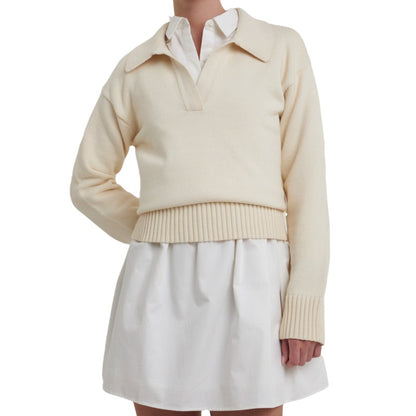 Woman styled in a custom cream cashmere polo sweater with a V-neck, worn over a white shirt and paired with a white skirt.