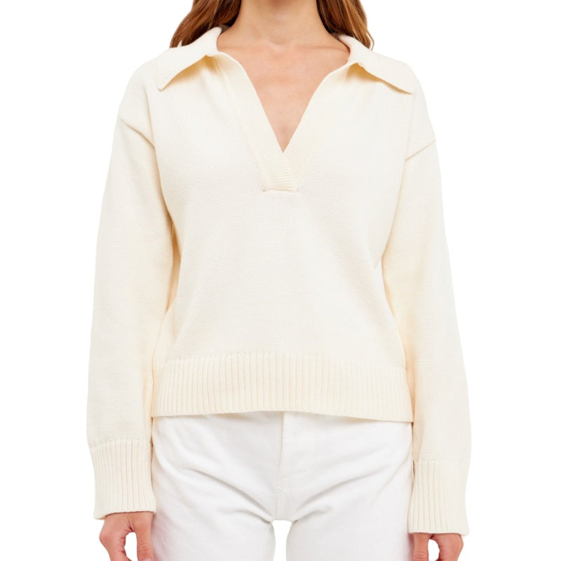 Woman wearing a custom cream cashmere polo sweater with a deep V-neck and relaxed fit, paired with white trousers.