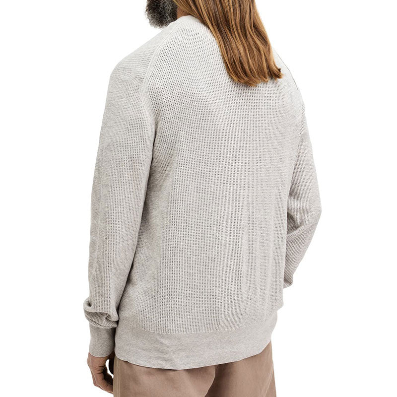 Back view of a light grey knit sweater made of 100% cotton, showcasing the sweater's texture and relaxed fit on the model.