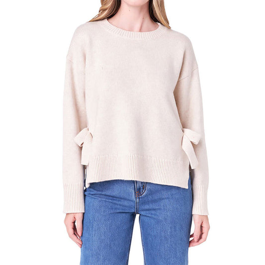 Front view of a custom oversized cotton blend knit sweater in beige, with side tie details, ribbed cuffs, and a cozy, relaxed fit.