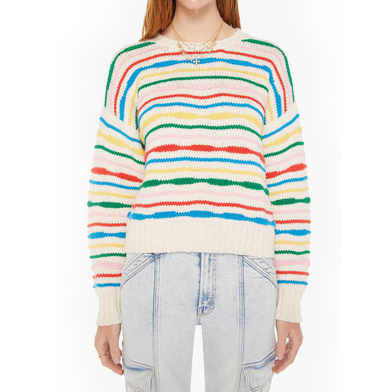 Front view of a person wearing a rainbow striped sweater. The sweater features horizontal stripes in various colors including green, blue, red, yellow, and pink on a white background. The person is also wearing light blue jeans and a gold necklace.