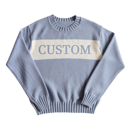 Light blue custom knit sweater with a white stripe across the chest displaying the word 'CUSTOM' laid out flat.