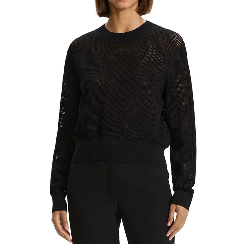 Woman wearing a black hollow out knit sweater, showcasing the see-through design, crewneck, long sleeves, and ribbed cuffs and hem.