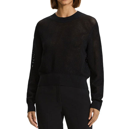 Woman wearing a black hollow out knit sweater, showcasing the see-through design, crewneck, long sleeves, and ribbed cuffs and hem.