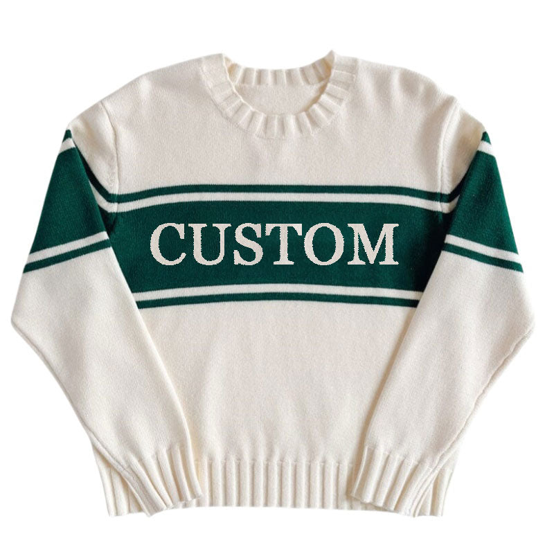 White custom knit sweater with green stripes across the chest and arms displaying the word 'CUSTOM' laid out flat.