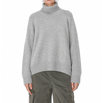 Woman wearing a grey high-neck knit pullover with dark trousers, front view.