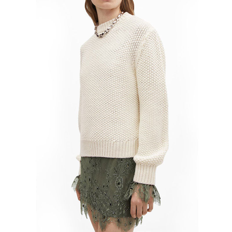 Side view of a model wearing a cream-colored, grid pullover sweater with a green lace skirt. The sweater has a textured knit pattern and ribbed cuffs.