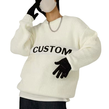 Person wearing a white oversized ribbed knit sweater with a custom logo printed across the chest, accessorized with a chain necklace and gloves.