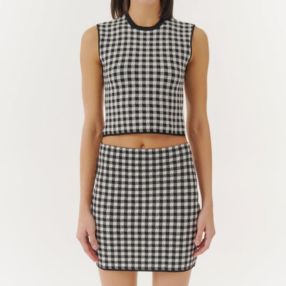 A woman wearing a black and white checkered sleeveless crop top and a matching high-waisted skirt. The background is a plain white color.