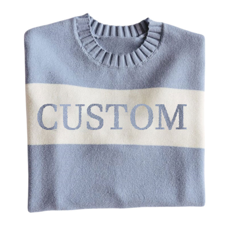 Folded light blue custom knit sweater with a white stripe across the chest displaying the word 'CUSTOM'.