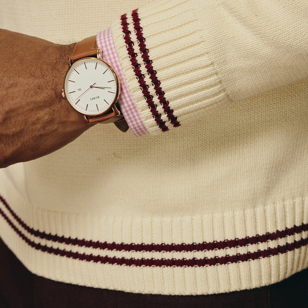 Close-up of a man's wrist showing a watch and the sleeve of a custom Greek embroidery sweater with maroon stripes.