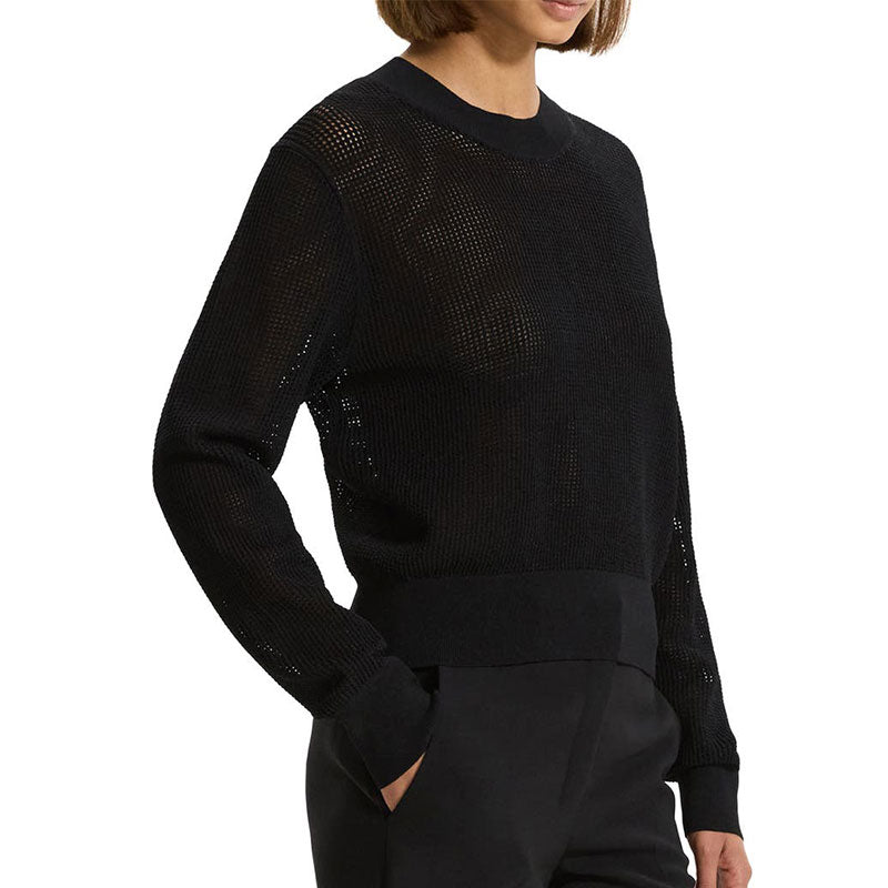 Side view of a black hollow out knit sweater worn by a woman, showcasing the see-through design, crewneck, long sleeves, and ribbed cuffs and hem.