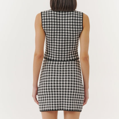 Back view of a woman wearing a black and white checkered sleeveless crop top and a matching high-waisted skirt, standing against a plain white background.