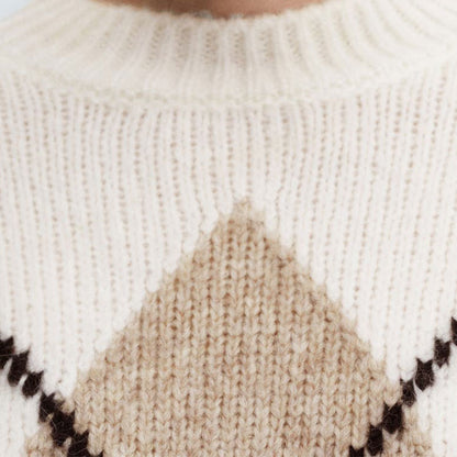 Close-up view of the cream-colored sweater showing the detailed knit texture and part of the beige and black argyle pattern on the front.