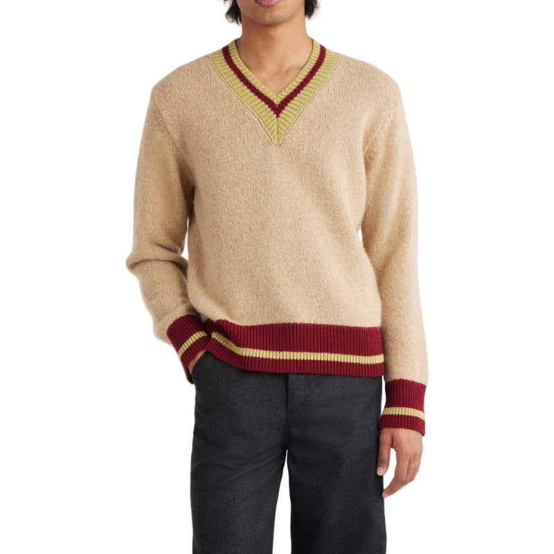 Man wearing a beige merino wool V-neck sweater with burgundy and gold striped accents on the cuffs and waistband, paired with dark trousers. The sweater showcases a soft texture and elegant style, ideal for custom knitwear collections.