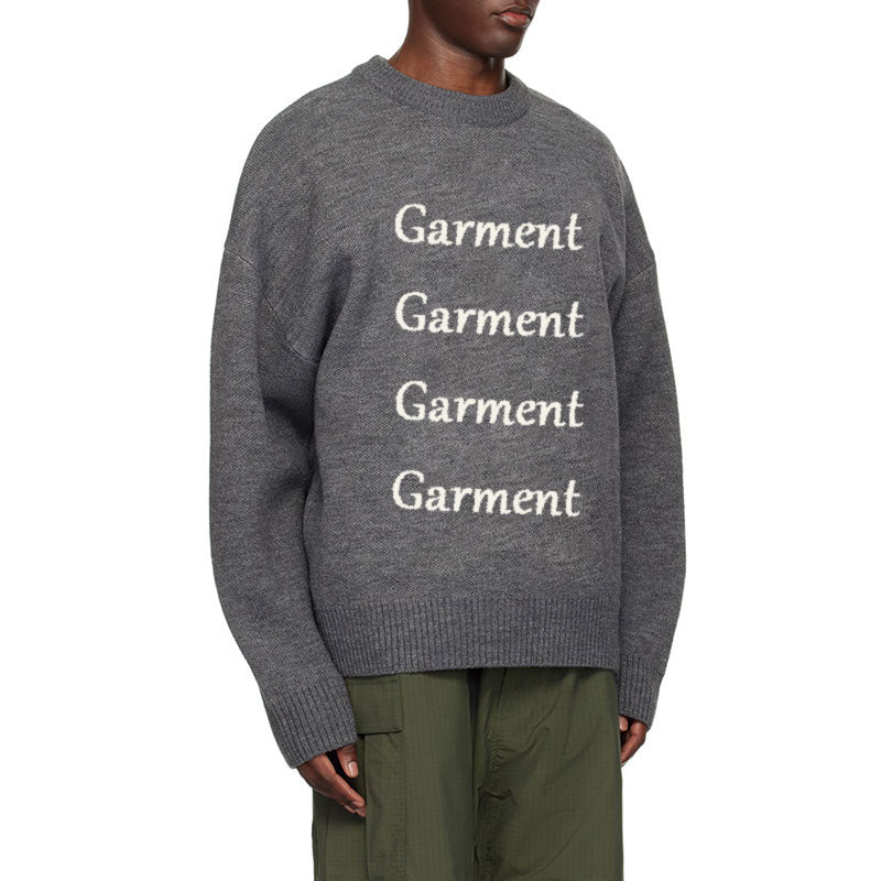 Side view of a custom gray jacquard knit sweater with repeated 'Garment' lettering on the front, showcasing the oversized fit and textured design.