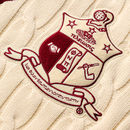 Close-up of embroidered crest on cream cable knit sweater