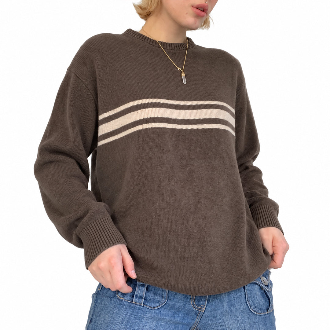 Woman wearing a brown sweater with cream chest stripes and blue jeans.