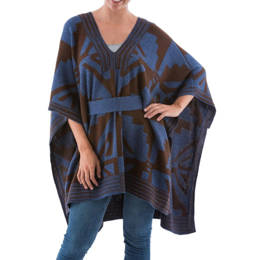 A person wearing a custom 100% acrylic poncho sweater in blue and brown, featuring a V-neck design and geometric patterns, styled with a belt at the waist.