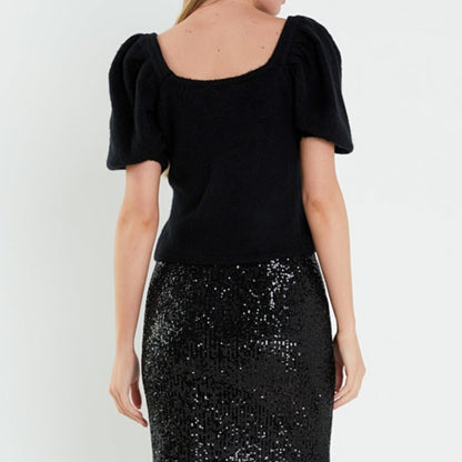 Back view of a woman wearing a custom 100% cotton puff sleeve square neck women's knitted sweater in black, paired with a black sequin skirt.