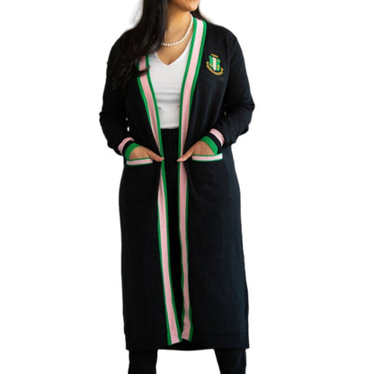Woman wearing a long, black acrylic cardigan with Greek-style embroidery, highlighted by pink and green stripes along the length and cuffs
