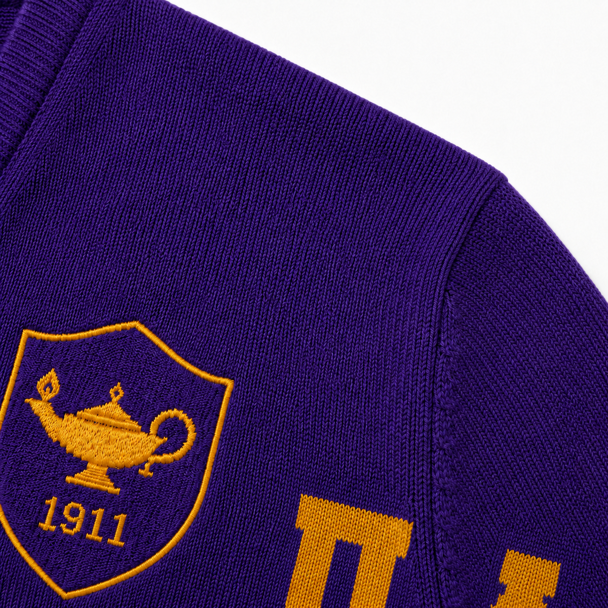Close-up purple knit texture with gold lamp shield, 1911 embroidery, jacquard stitches and shoulder seam