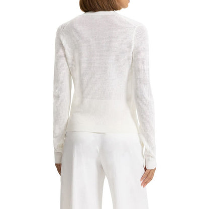 Back view of a woman wearing a custom crochet acrylic knit sweater in white. The cardigan has a seamless design at the back, showing its breathable, lightweight texture. She pairs it with white pants.