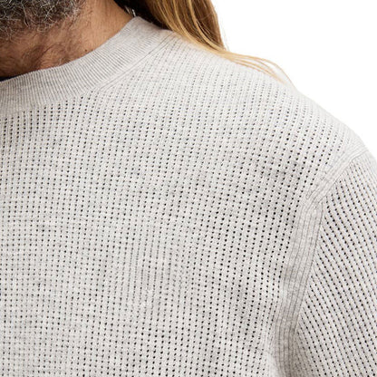 Close-up view of the light grey knit sweater's texture, highlighting the detailed and high-quality knitting pattern of the 100% cotton material.