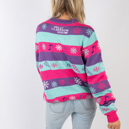 Back view of a custom cozy cashmere Christmas sweater featuring a 'Happy Holidays Y'all' design and 'The Kelly Clarkson Show' logo in purple, pink, teal, and white colors. The sweater includes holiday motifs like snowflakes and musical notes, perfect for festive celebrations.