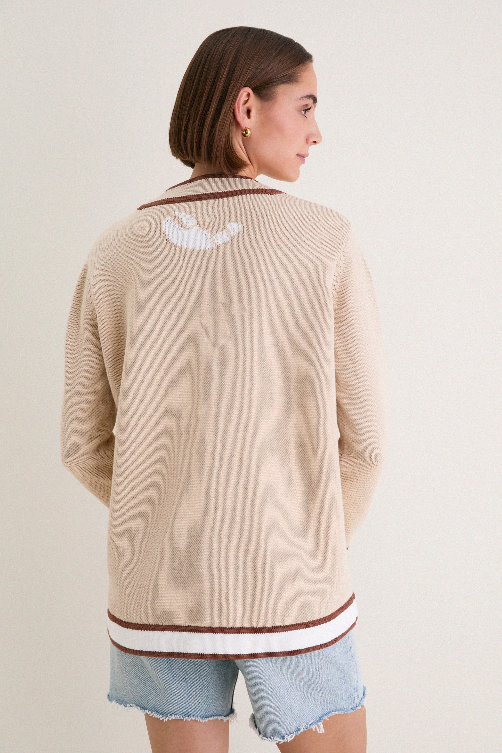 Back view of beige knit cardigan with simple design and contrast hem detail.
