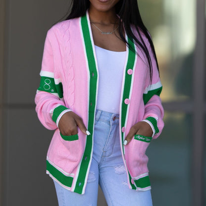 Stylish young woman standing outdoors wearing a custom pink and green striped cotton cardigan over a white top and ripped blue jeans. The cardigan is adorned with vibrant pink buttons and '08' numbering on the sleeve, showcasing a modern, chic style.