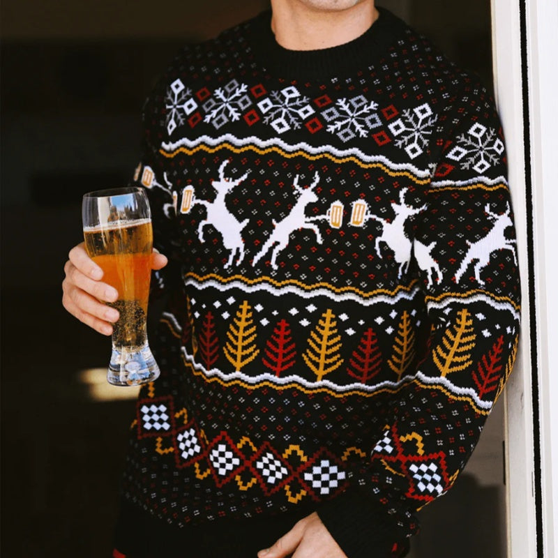 Close-up of a man wearing a festive ugly Christmas sweater with reindeer and beer mug designs, holding a glass of beer. The sweater features bold, colorful patterns in red, yellow, black, and white.