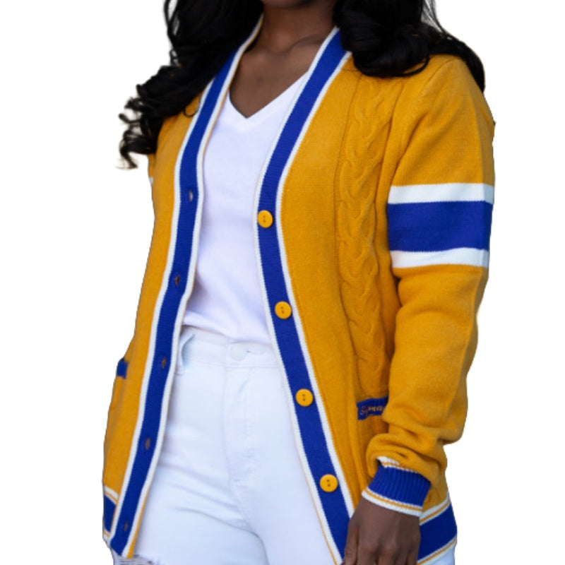 A person wearing a yellow cardigan with blue and white stripes on the sleeves and edges, featuring yellow buttons. The cardigan is styled with a white v-neck shirt and white pants, showcasing a custom Greek design ideal for fraternities or sororities.