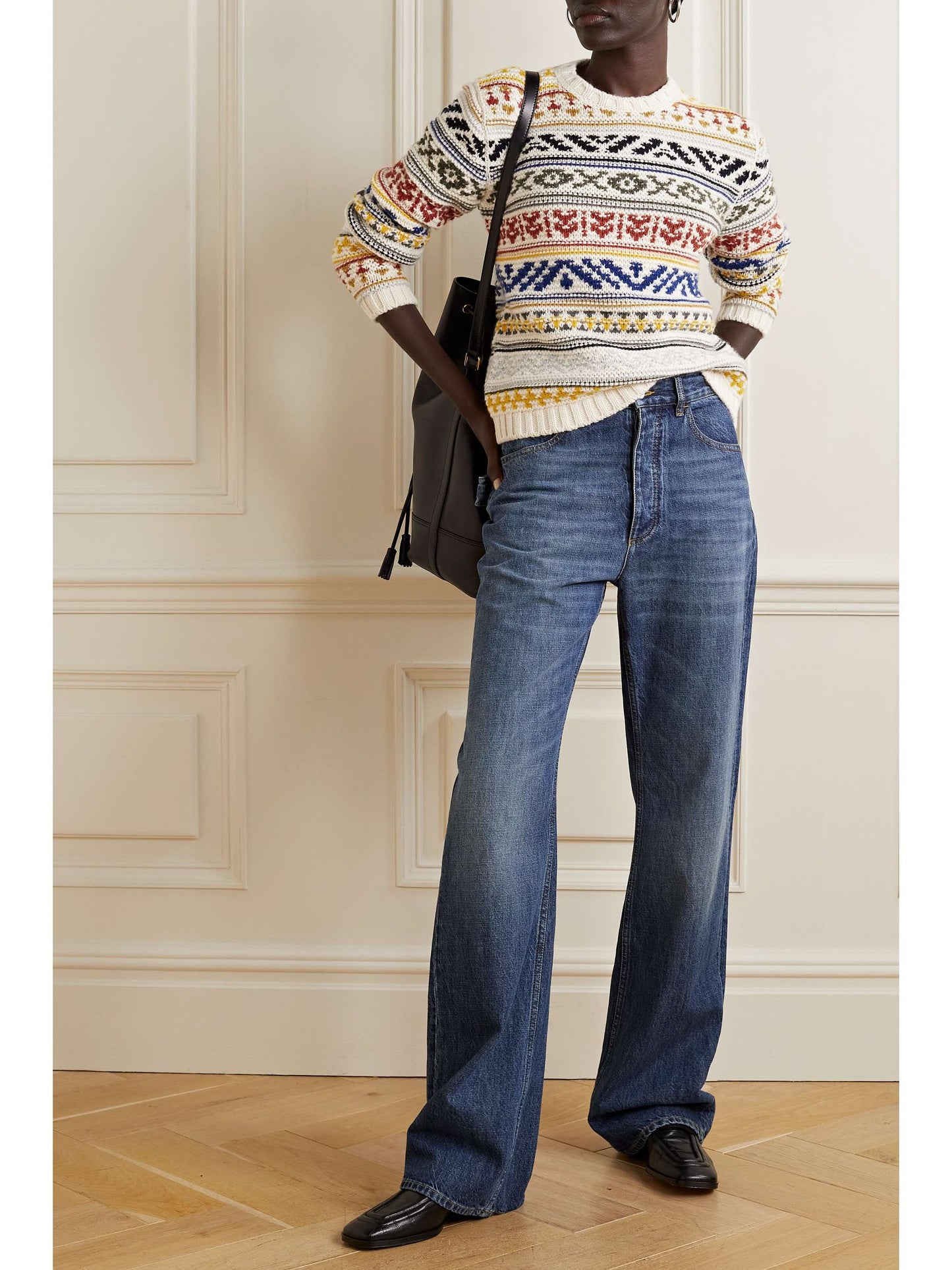 "Model wearing a custom 100% cotton women's sweater with a colorful Fair Isle pattern, paired with high-waisted blue jeans. The sweater features intricate knit designs in red, blue, yellow, and green on a cream background. The model is posing with one hand in the pocket."